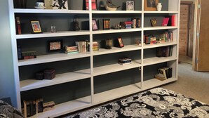 Ein großes, weißes Bücherregal mit mehreren Ablagen, gefüllt mit Büchern, gerahmten Bildern und Dekorationsobjekten.