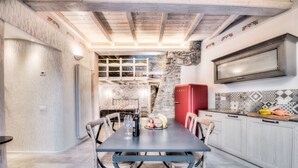 Un coin repas comprenant une table, des chaises, un réfrigérateur rouge et une cuisine dont le sol est recouvert de carreaux décoratifs.