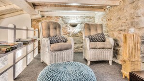 Une pièce chaleureuse avec deux fauteuils en osier, un pouf rond et une bibliothèque.