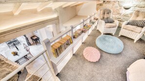 Un coin lecture confortable avec des étagères à livres, des fauteuils en osier et un mur en pierre.