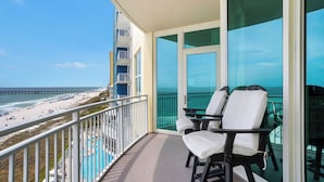 Un balcone con due sedie e un tavolo, affacciato su una spiaggia e un molo.