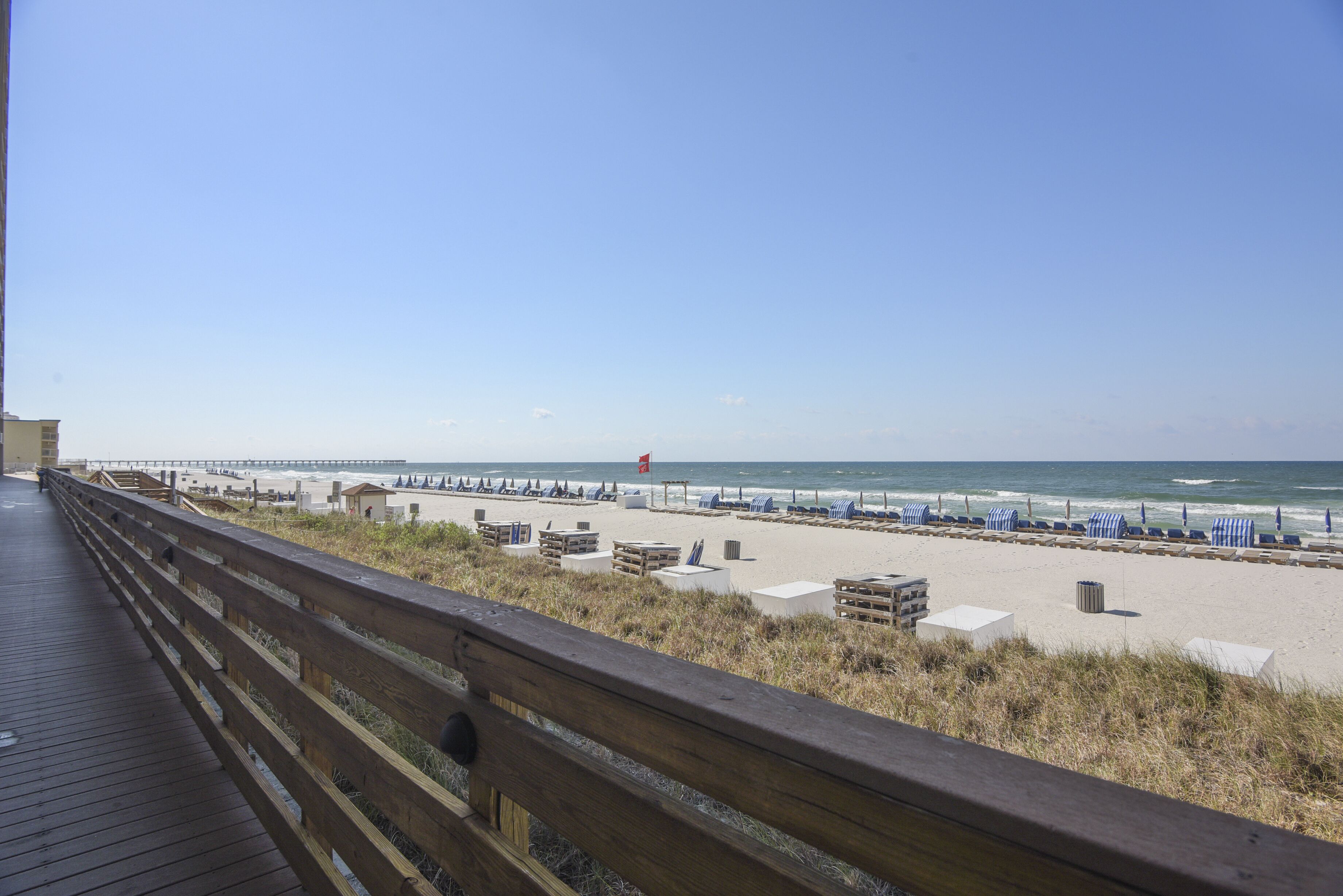 A wooden boardwalk leading to a beach with beach chairs and umbrellas.
