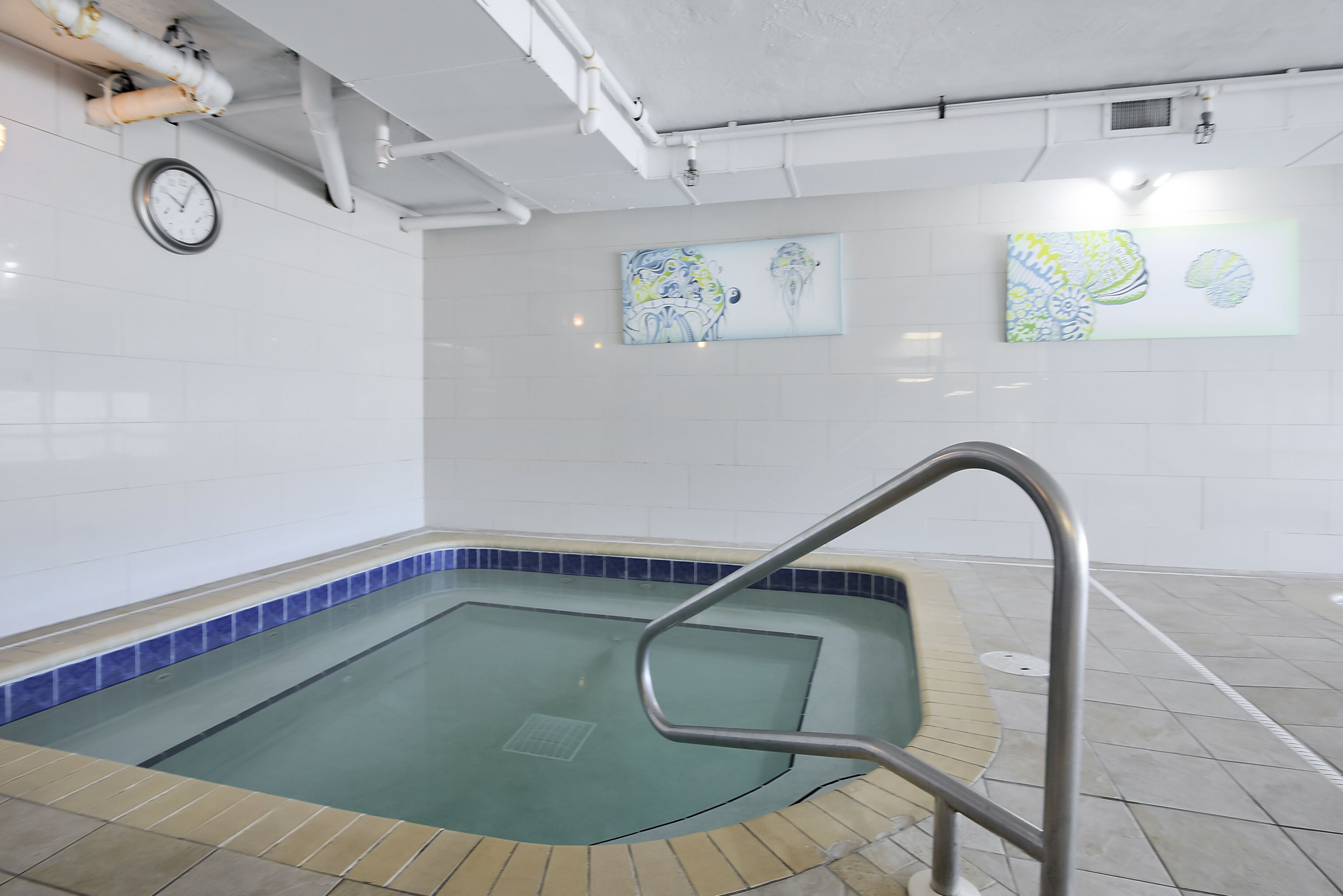 Ein Pool mit einer Fliesenkante, einer Metallleiter und zwei abstrakten Gemälden an der Wand.