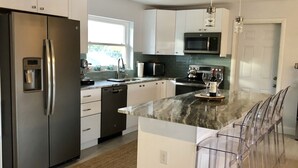 Eine moderne Küche mit einem Edelstahl-Kühlschrank, einem eingebauten Geschirrspüler, einer Mikrowelle und einer großen Kochinsel mit Barhocker.