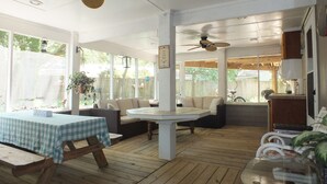 A covered patio area with wooden flooring, a table with a checkered tablecloth, and two sofas. - BEACH GETAWAY W/ JACUZZI TUB & GAME ROOM CENTRALLY LOCATED SPACIOUS ROOMS (Kill Devil Hills)