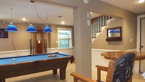 A pool table with blue lamps, a pool cue, and a chair with a patterned cushion. - BEACH GETAWAY W/ JACUZZI TUB & GAME ROOM CENTRALLY LOCATED SPACIOUS ROOMS (Kill Devil Hills)
