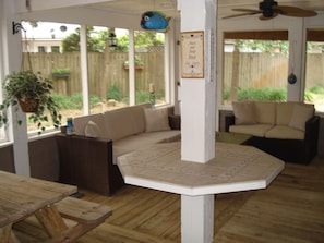 A covered patio area with a wooden table, cushioned seating, and a ceiling fan.