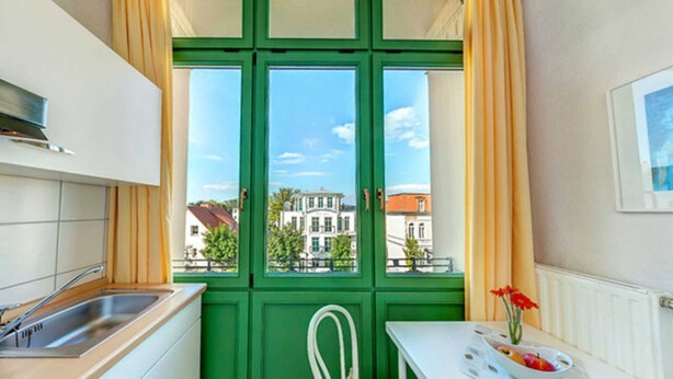 Een keuken met een groen raam, een witte spoelbak, en een tafel met een bloevas.
