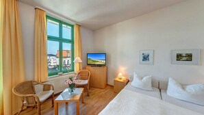 Een hotelkamer met een bed, een televisie, een bureau, twee stoelen, een raam met gordijnen en twee ingelijste foto's aan de muur.