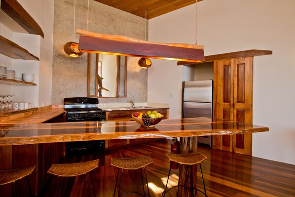 Una cocina moderna con una isla grande, taburetes de bar, un refrigerador de acero inoxidable y una lámpara colgante.