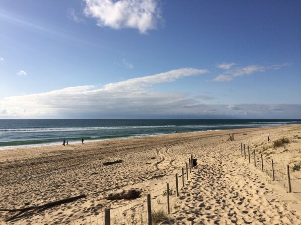 Une plage de sable avec une clôture en bois et un ciel dégagé.