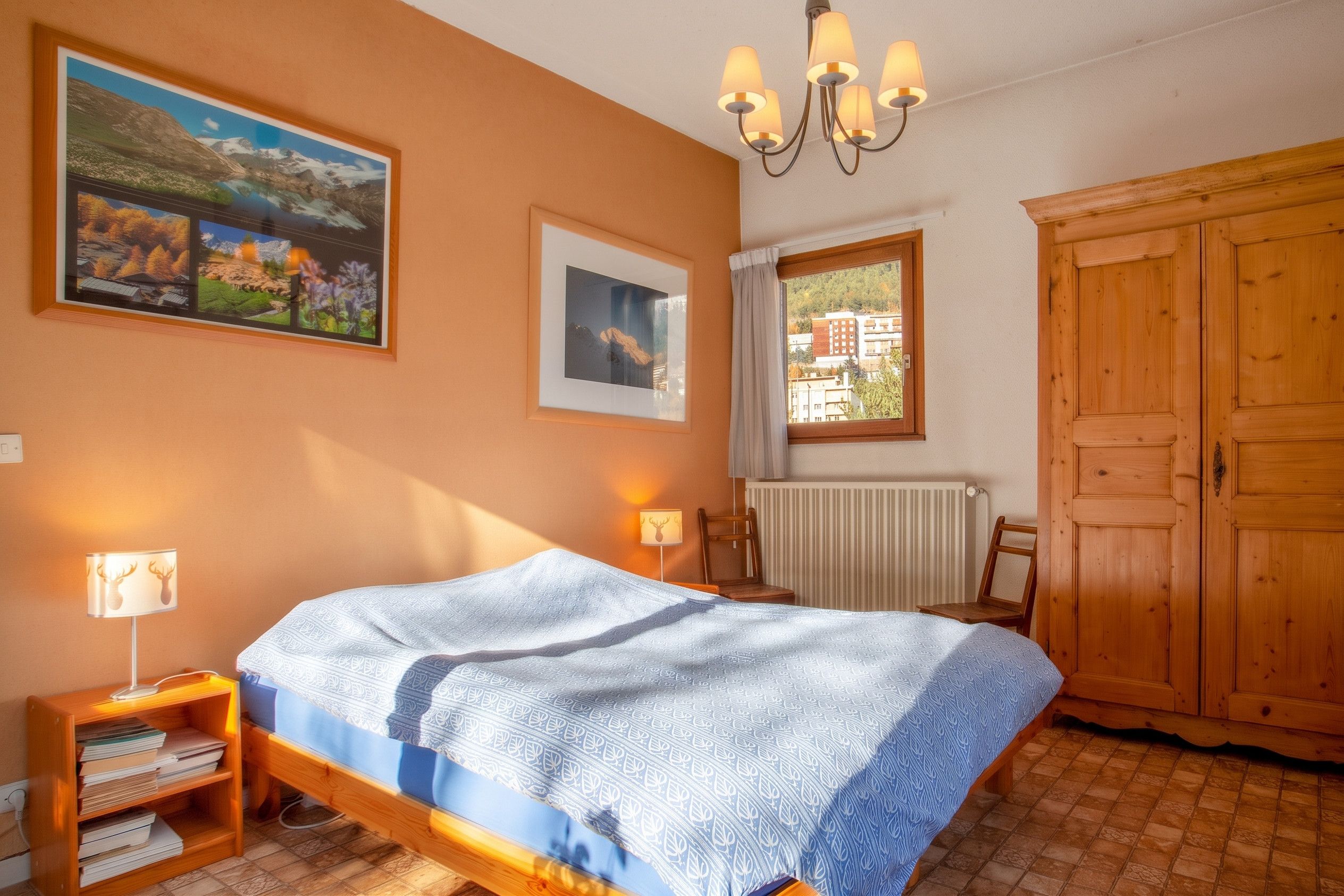Une chambre à coucher comprenant un lit, une armoire en bois, un radiateur, une fenêtre avec vue et deux lampes fixées au mur.