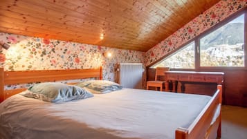 Ein Schlafzimmer mit Holzboden, einem Bett mit Kissen, einem Nachttisch, einem Fenster mit Blick und floralem Wandpapier.