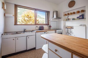 A kitchen with white cabinets, a wooden countertop, a window with a view of trees, and shelves with kitchen items. - Homerez - Chalet in Briançon (Briançon)