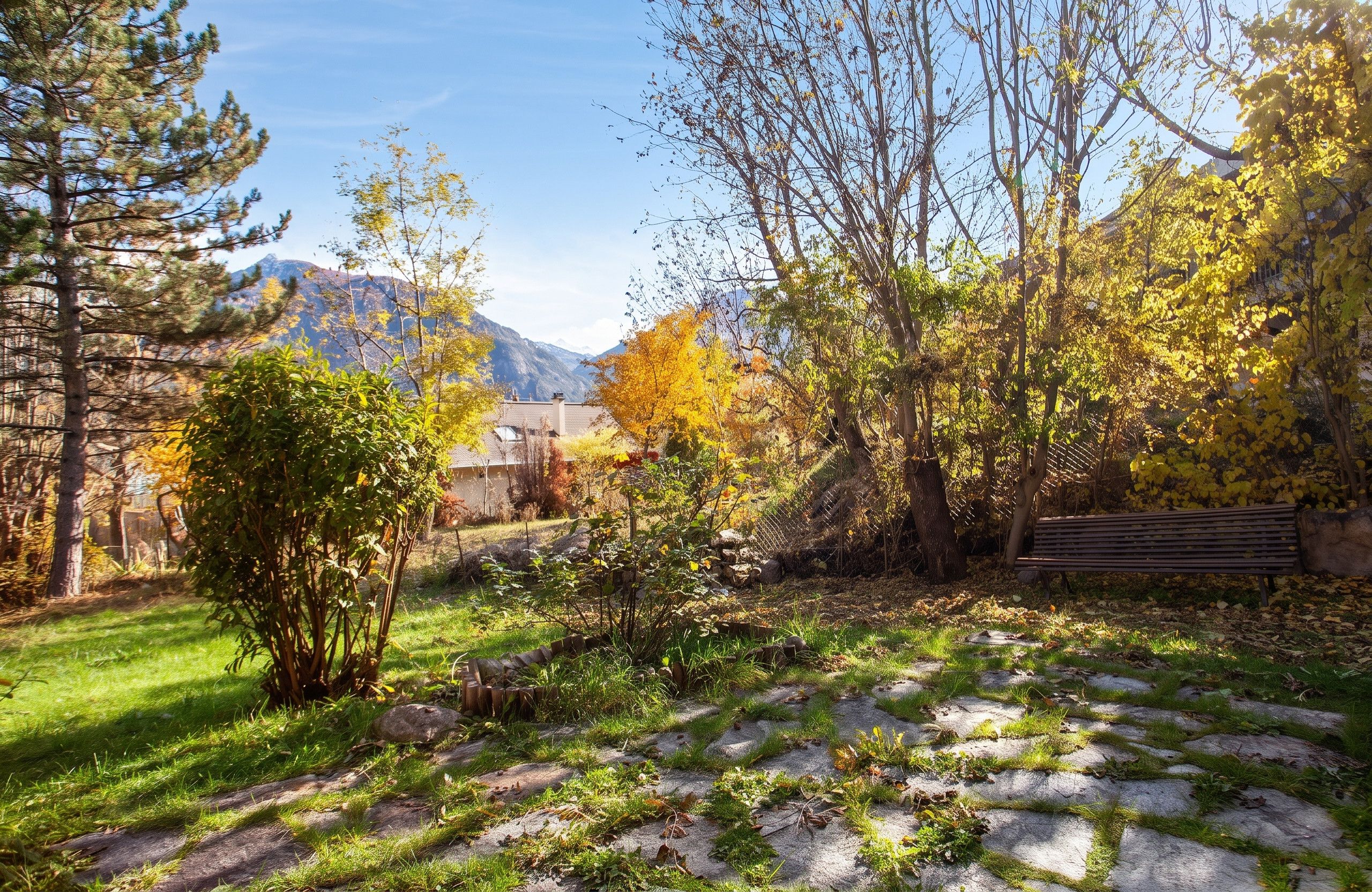 Ein Garten mit einem Kiesweg, Bäumen im Herbstlaub und einem Berg im Hintergrund.