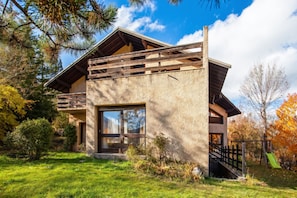 Une maison moderne avec une façade en pierre, de grandes fenêtres et une terrasse en bois.