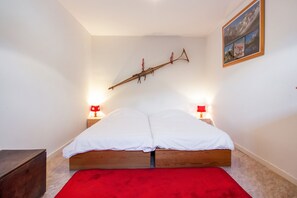 A bedroom with a wooden bed, two bedside lamps, a red rug, and a framed picture on the wall. - Homerez - Chalet in Briançon (Briançon)