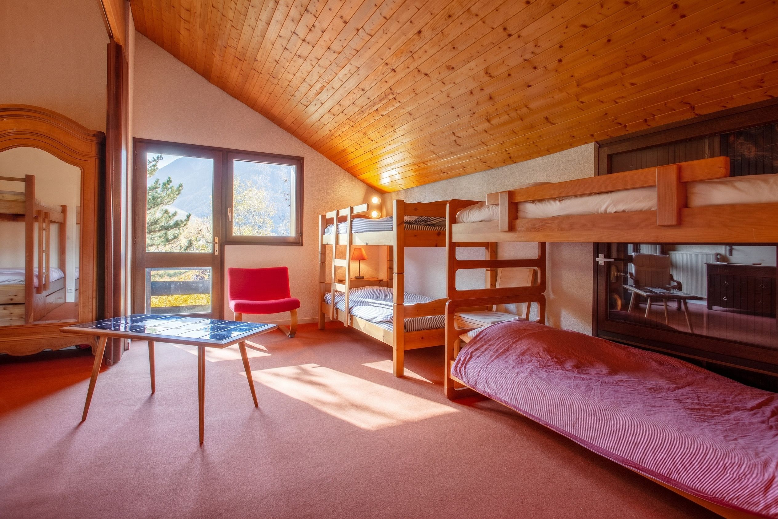 Een kamer met stapelbedden, een rode stoel en een tafel.