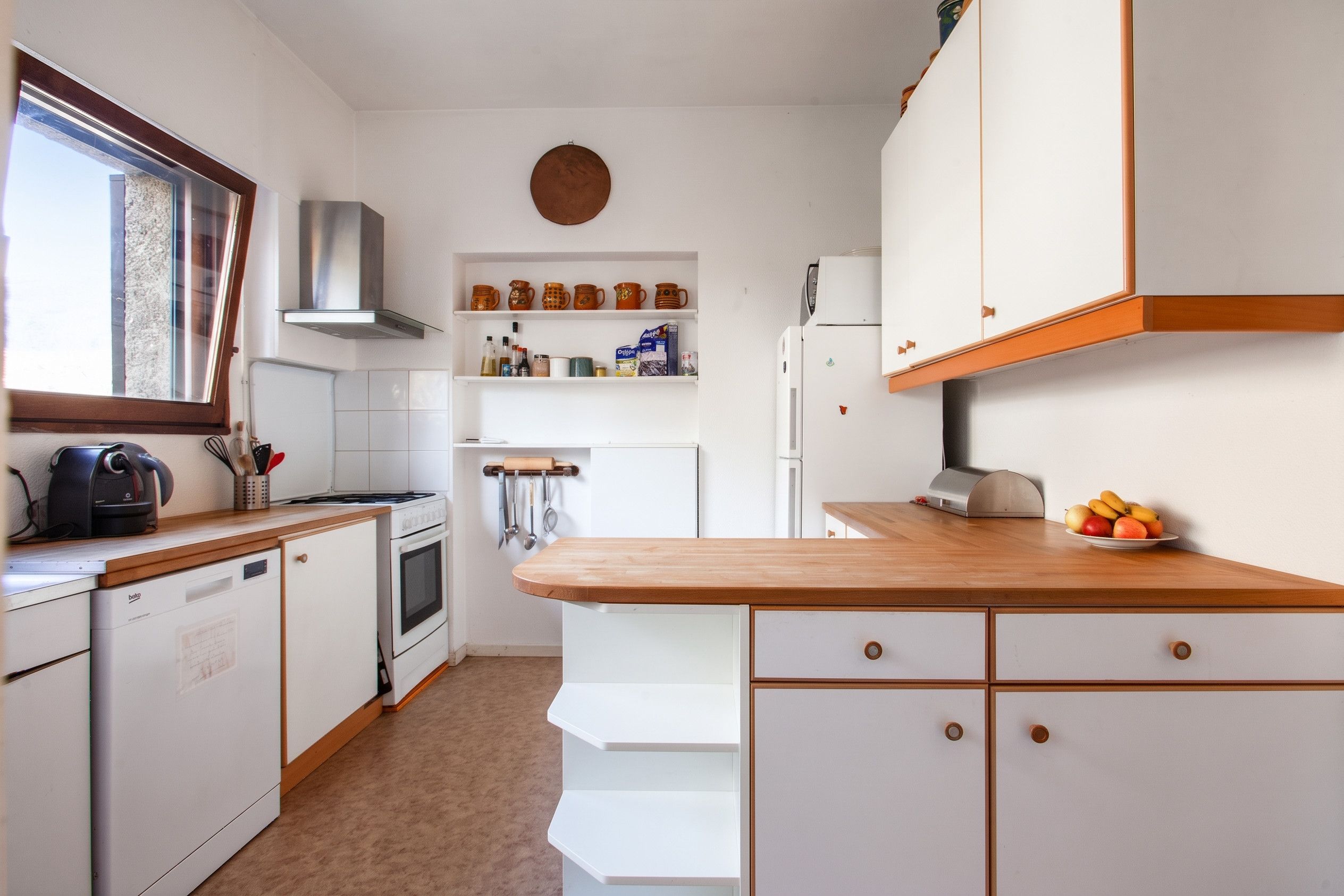 Een kleine keuken met witte kastjes, een houten aanrechtblad en een inbouwoven.