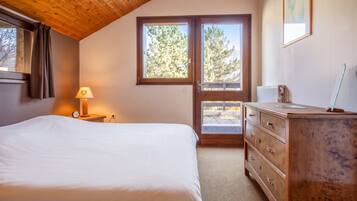 A bedroom with a bed, a dresser, a lamp, and a window with a view of trees.