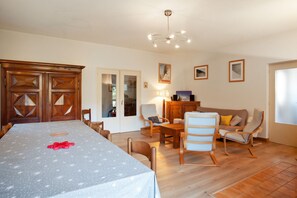 A dining area with a table set for four, a wooden cabinet, and a sofa in a living room. - Homerez - Chalet in Briançon (Briançon)