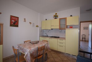 A small kitchen with yellow cabinets, a dining table with chairs, and a refrigerator.