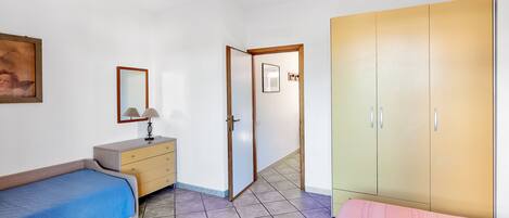 Ein Schlafzimmer mit einem Bett, einem Schminktisch, einem Kleiderschrank und einer Tür zu einem anderen Raum.