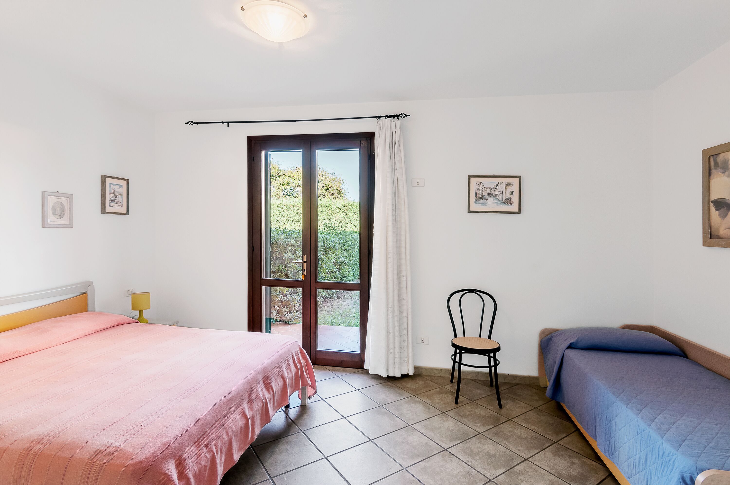 Ein Zimmer mit zwei Betten, einem Sessel und einem fenster mit Vorhängen.
