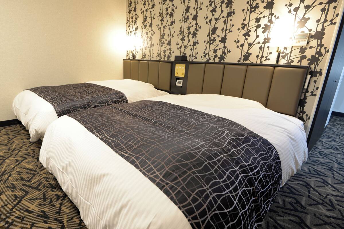 A hotel room with two beds, a patterned carpet, and a wall with a floral design.
