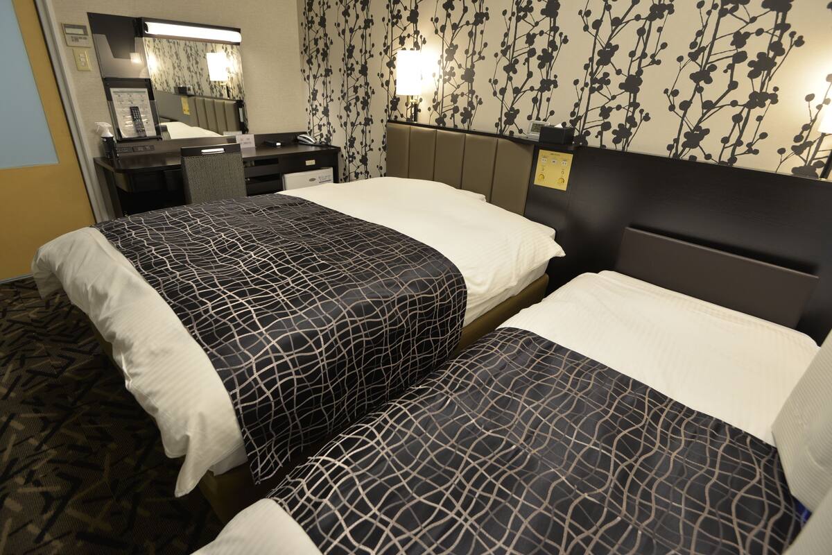 A hotel room with two beds, a desk with a telephone, a mirror, and a wall with a floral pattern.
