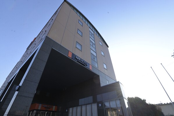 Un edificio de varios pisos con un cartel que dice "APA HOTEL" en la fachada.