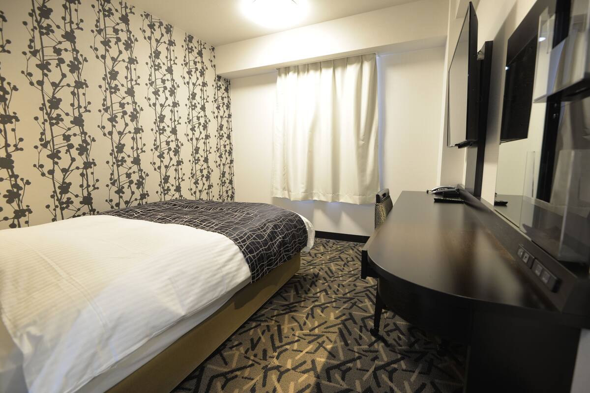 A hotel room with a bed, a desk, a chair, and a large mirror.
