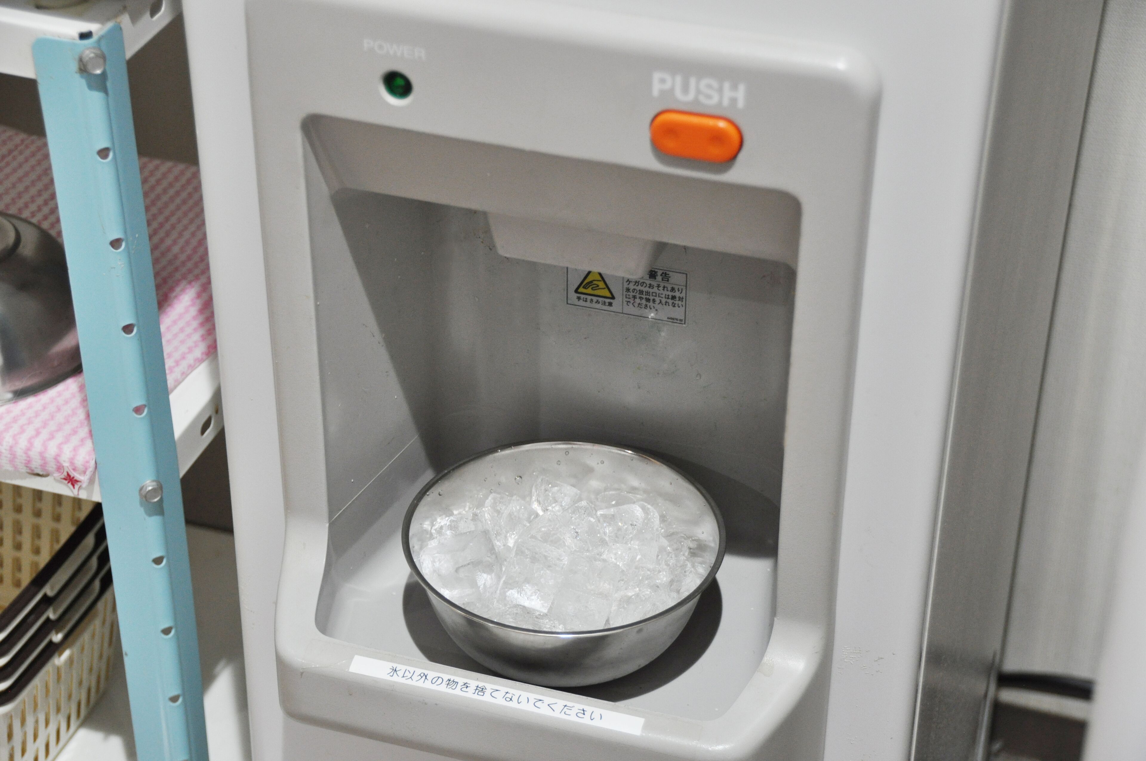 Un distributeur de glaçons à bouton-poussoir, muni d’une étiquette d’avertissement et d’un récipient en métal rempli de glaçons.