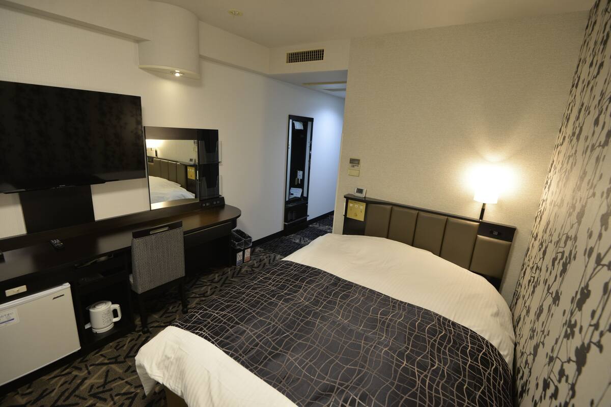A hotel room with a large bed, a desk with a flat-screen TV, a coffee maker, and a small refrigerator.