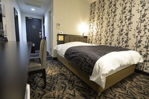 Habitación de hotel con cama, escritorio y silla. Se ve una puerta y una pared con estampado floral.