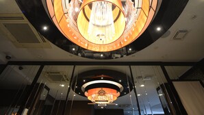 Un candelabro con múltiples fuentes de luz y diseño circular, suspendido del techo en una luminosa zona de recepción.