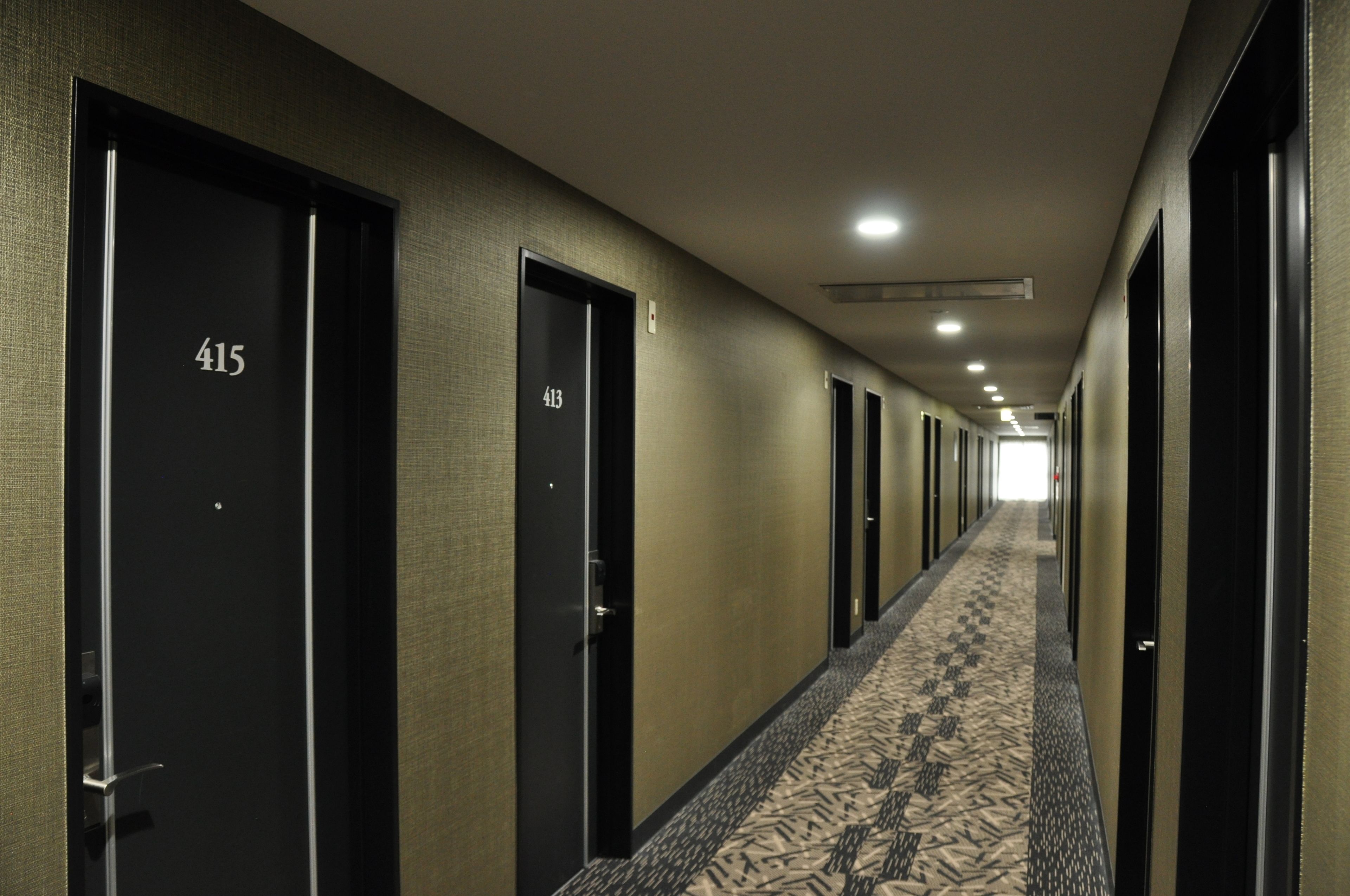 A hotel hallway with doors numbered 415 and 413, carpeted with a geometric pattern, and a ceiling with recessed lighting.