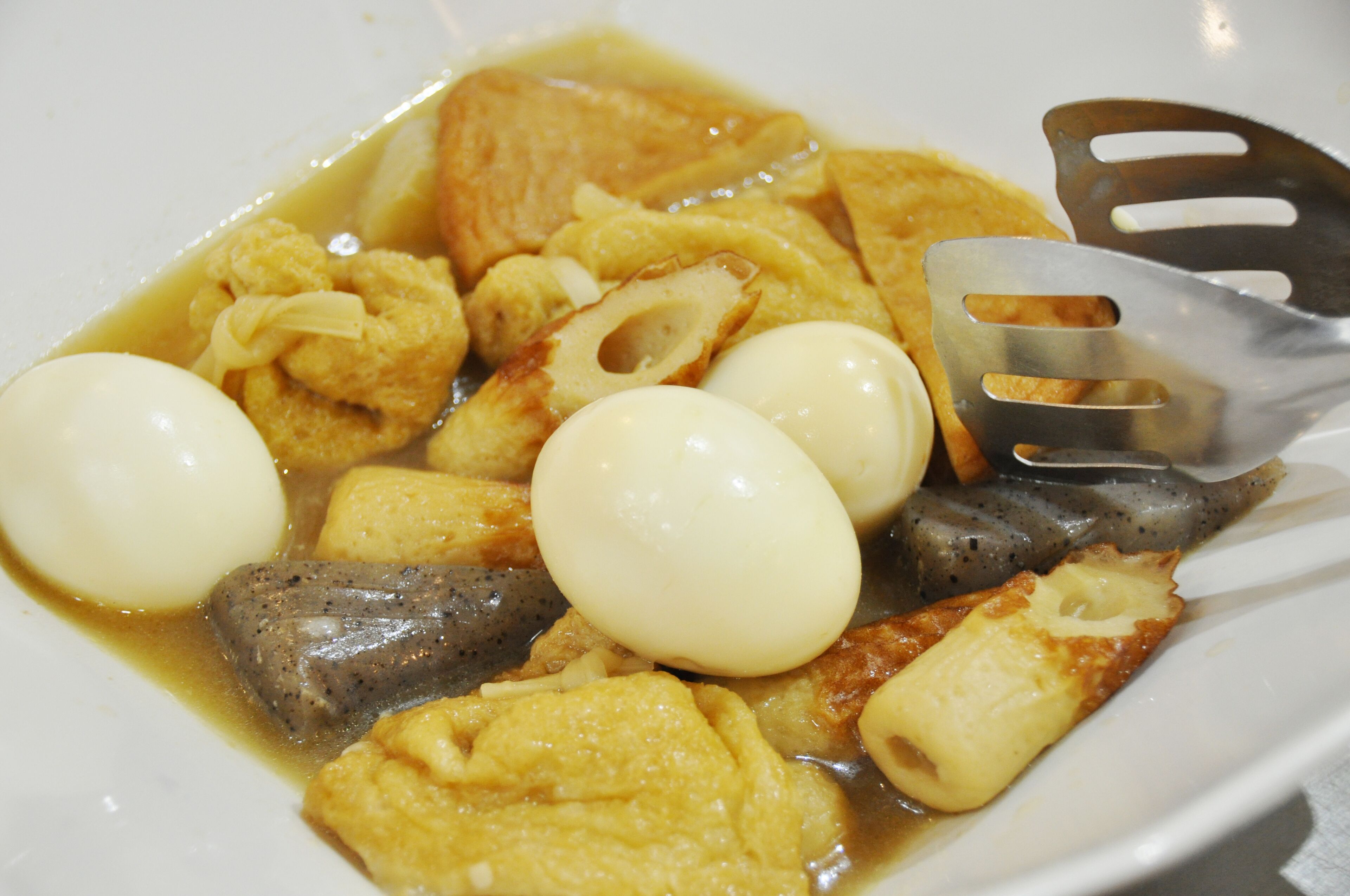 En tallrik med mat som innehåller olika ingredienser, bland annat ägg, kött och grönsaker, serverat i en buljong.