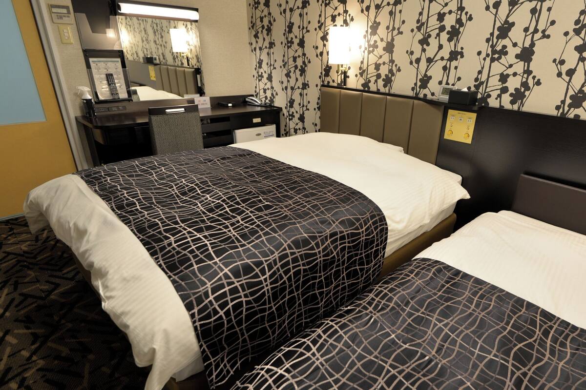 A hotel room with two beds, a desk, a mirror, and a wall with a floral pattern.
