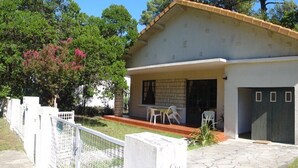 A two-story house with a tiled roof, a front porch with chairs, and a garage. - Villa Lagoon by Agence Bru - 2433 (Lacanau)