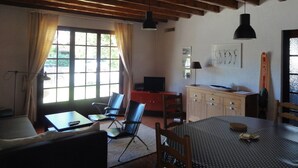 A room with a wooden ceiling, a dining table with chairs, a TV, a desk with a computer, and a window with curtains. - Villa Lagoon by Agence Bru - 2433 (Lacanau)