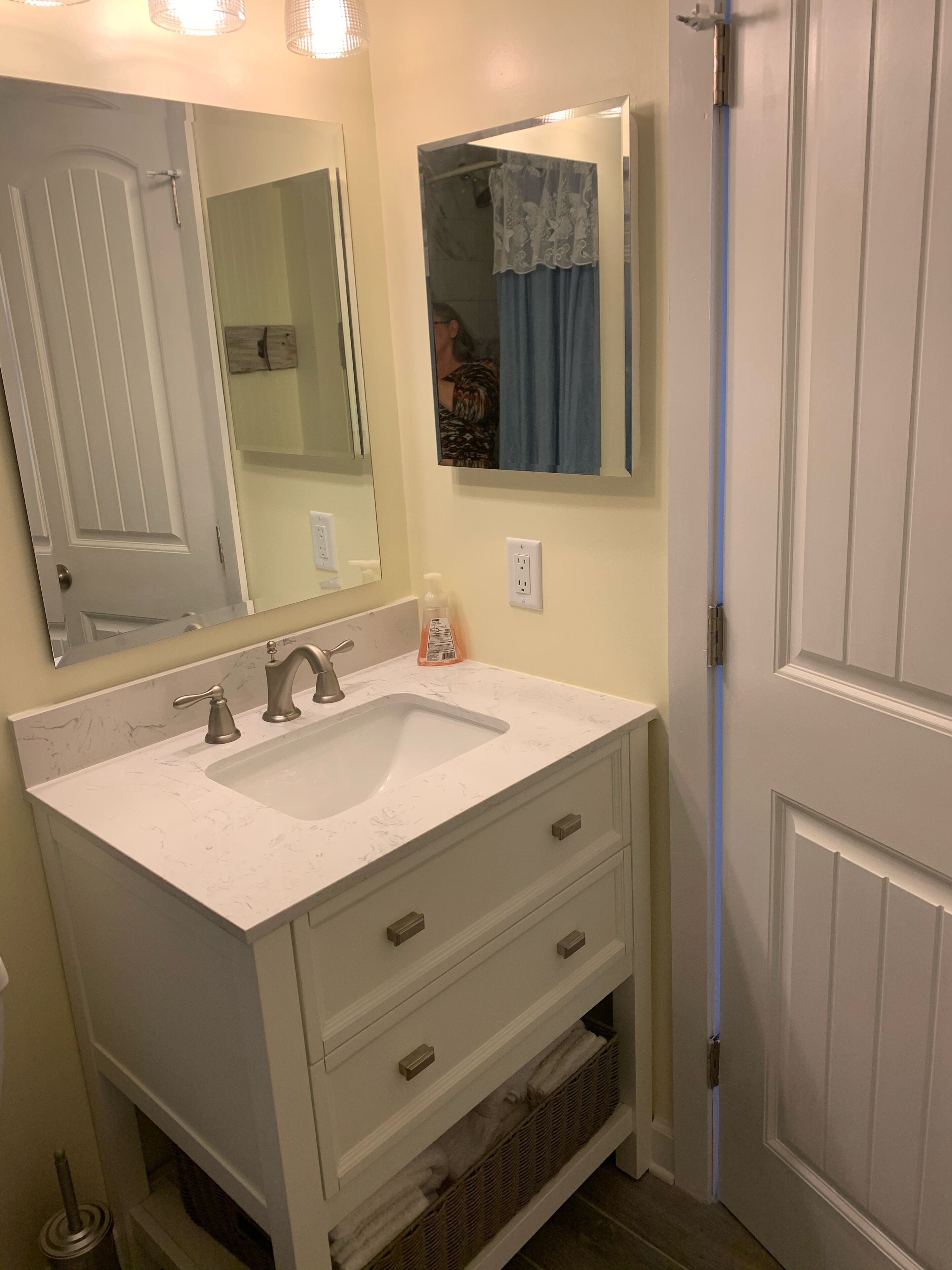 A bathroom with a white vanity, a large mirror, a sink, and a door.