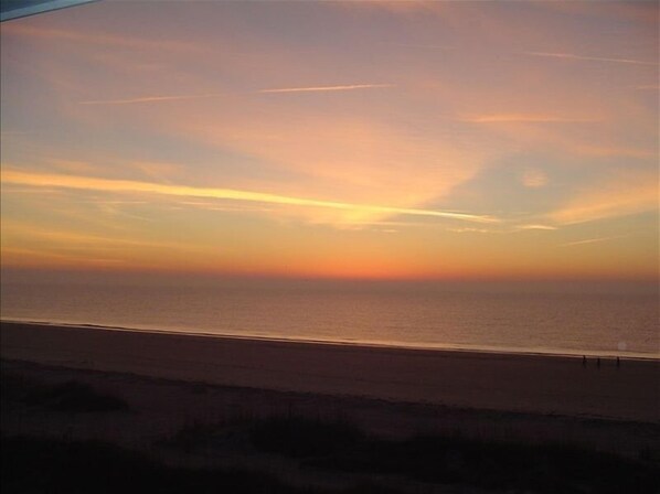 Une plage au coucher du soleil, avec un ciel dégagé et une mer calme.