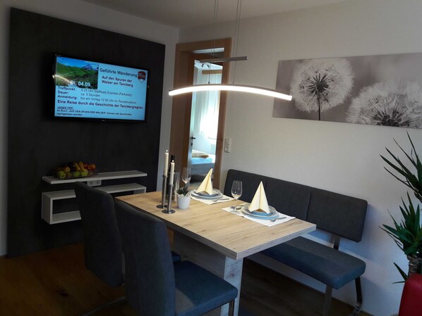 A modern dining area with a wooden table, blue chairs, a bench, and a TV displaying a guide for a walking tour. - Top 4 - House Annette (Schröcken)