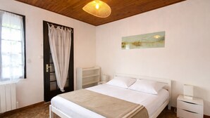 Un dormitorio con cama, una mesita de noche, cortinas en una ventana, techo de madera y una obra de arte colgada en la pared.
