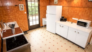 Una cocina con estufa, refrigerador, microondas y ventana con vista a follaje.