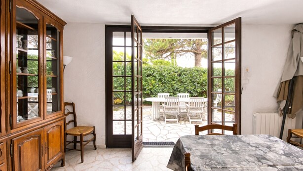 Una habitación con cama, un armario de madera y una mesa con sillas. Hay una puerta que da a un patio exterior con mesa y sillas.