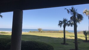 A view from a covered porch overlooking a grassy area with palm trees and a beach in the distance.