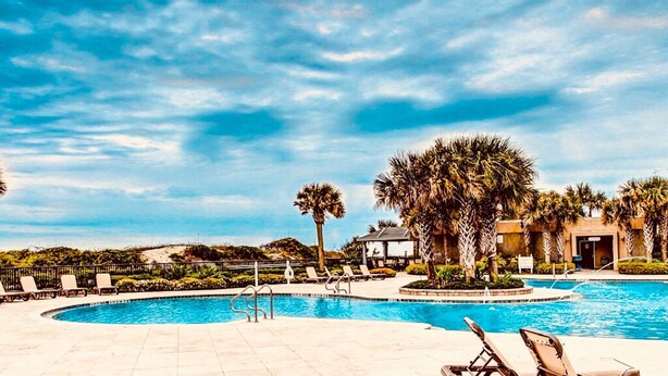 A swimming pool with lounge chairs and palm trees.