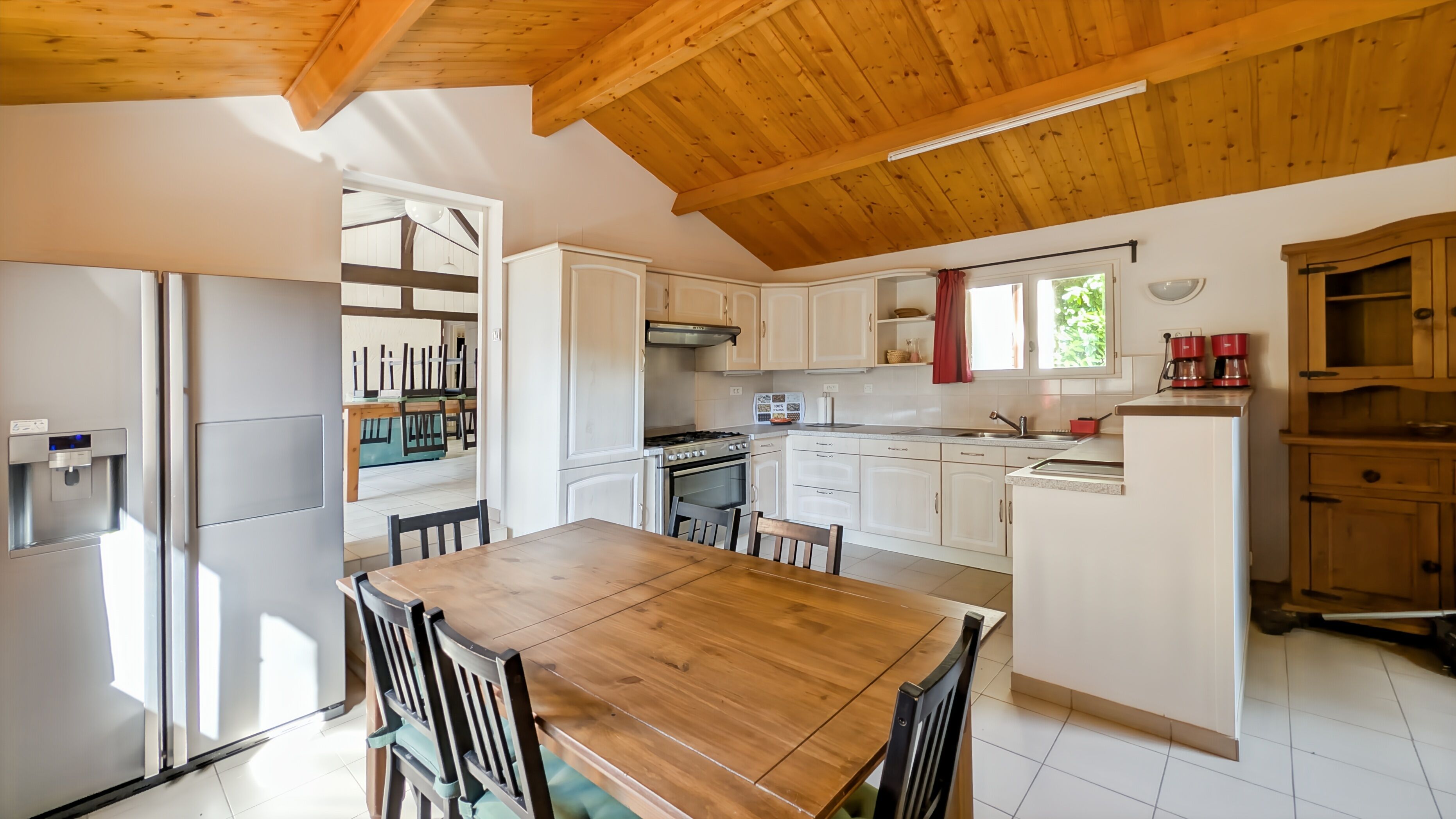 Une cuisine avec des meubles blancs, une table à manger en bois et un four encastré.